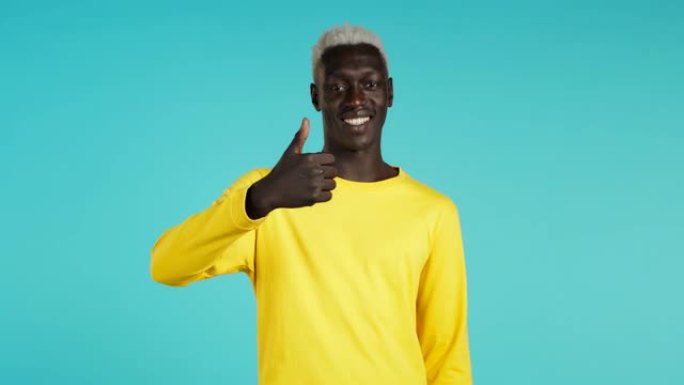 非裔美国人对镜头微笑。竖起大拇指的家伙，就像蓝色背景上的标志。赢家。成功。肢体语言。