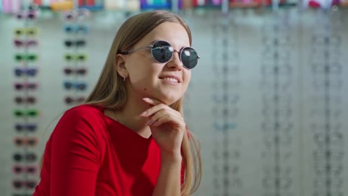 穿着时髦太阳镜的漂亮女孩。微笑的年轻女子在眼镜店模糊的背景上试戴新的黑色眼镜。