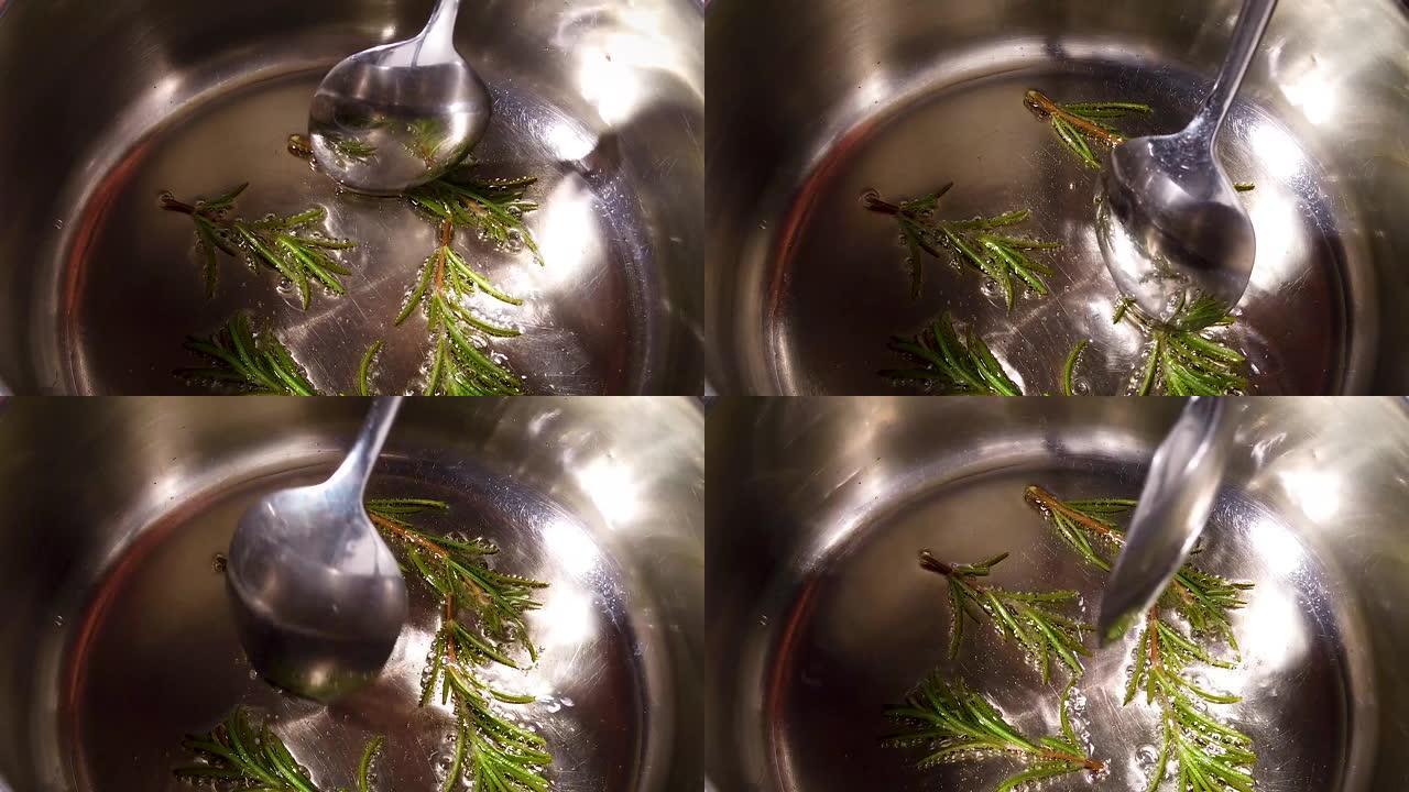 慢动作高角度勺子移动新鲜迷迭香树枝在不锈钢锅中的热油中嘶嘶作响