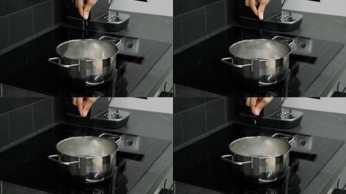 手指向水中加盐，关闭侧视图。烹饪过程。女性在智能厨房的锅里用开水添加香料。准备菜肴的过程