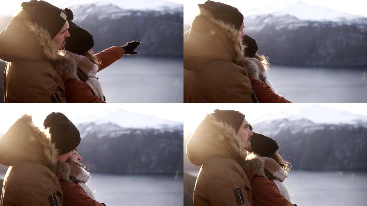 穿着冬装的年轻夫妇拥抱着，人们拥抱着在湖泊和山峰上的壮丽景色。欣赏美丽的山地自然景观。侧视图