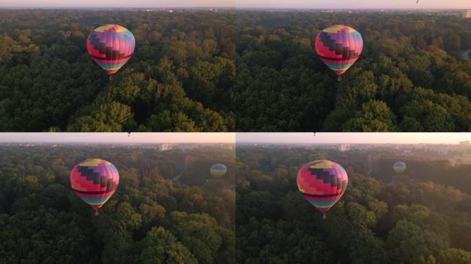 夏季日出时在欧洲小城市绿色公园和河流上空飞行的彩色热气球的空中无人机视图
