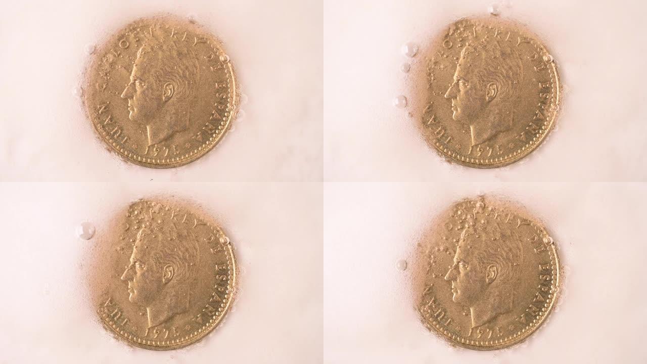 西班牙国王名誉胡安·卡洛斯一世的狮身人面像的旧比塞塔硬币在泡沫和气泡之间被清洗，象征着他遗产的退化
