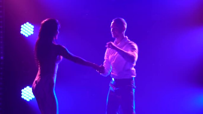美丽的一对专业艺术家跳舞热情的萨尔萨舞。年轻夫妇在黑暗的工作室里，在蓝色的光线中跳舞桑巴舞、伦巴舞、