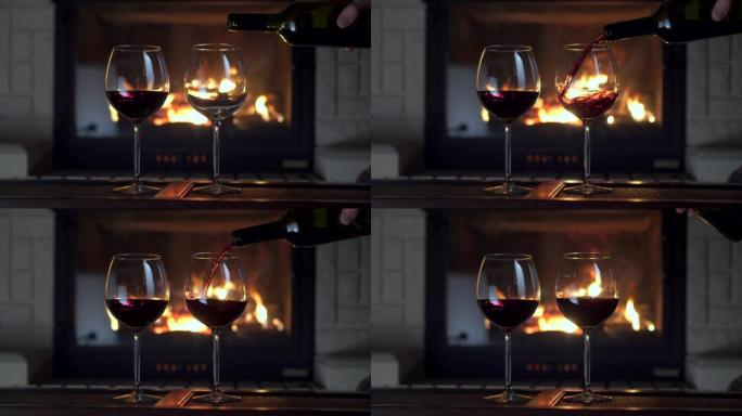 男性手将红酒从瓶子里倒入壁炉的两个玻璃高脚杯火焰中