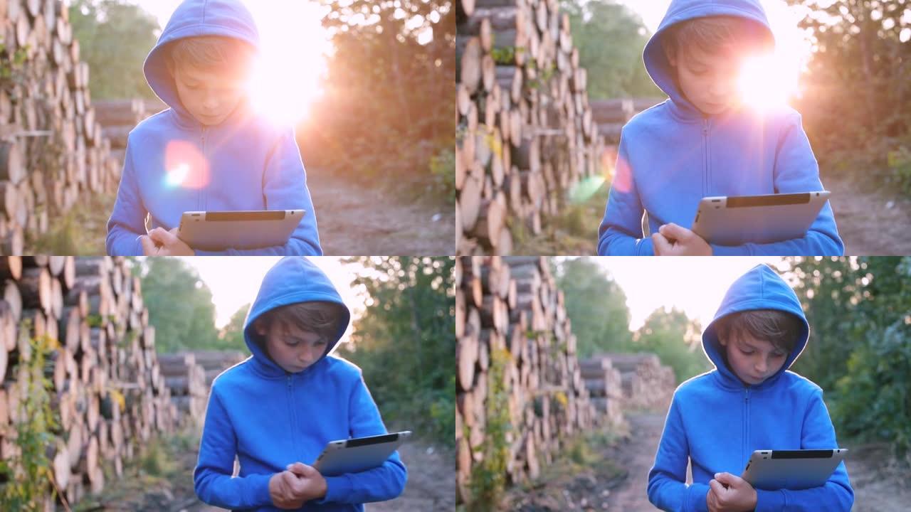 手拿平板电脑的男孩走过城市公园，看着小工具的屏幕。