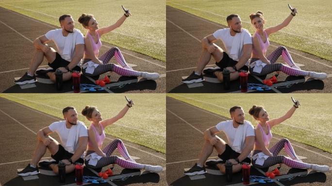 一对夫妇坐在体育场的跑步机上时在手机上自拍