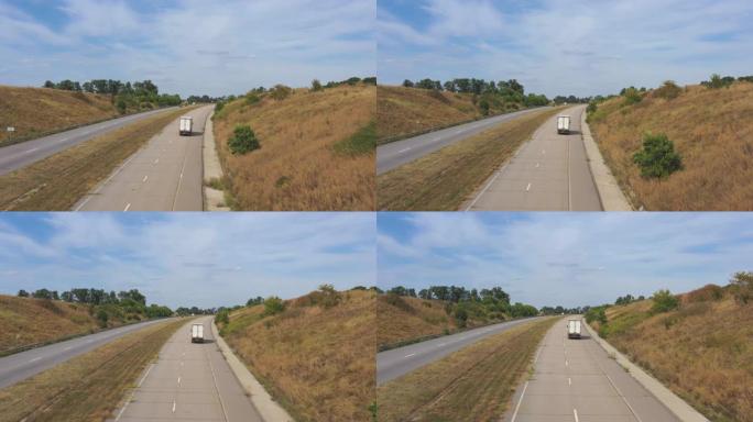在高速公路上行驶并运输货物的卡车与货运拖车的空中射击。在晴天通过乡村高速公路行驶的送货卡车的摄像头。