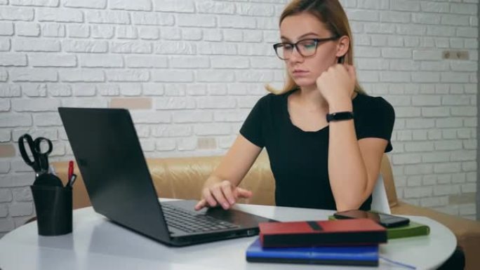 疲倦困倦的高加索年轻女子在家里用笔记本电脑工作时打哈欠并入睡。戴眼镜的金发女孩晚上在笔记本电脑上工作