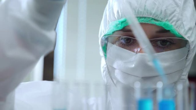 使用无菌测量移液管和滴液在试管中使用防护服和眼镜的女性实验室研究人员的特写镜头。集中化学家在实验室进