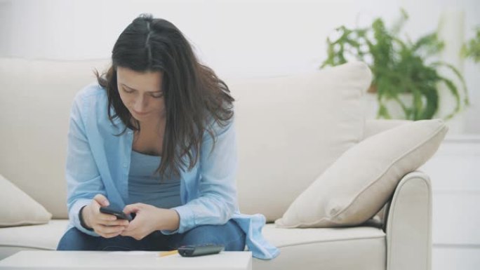 令人钦佩的女人正专注于在家中坐在沙发上使用智能手机。慢动作。复制空间。4K。