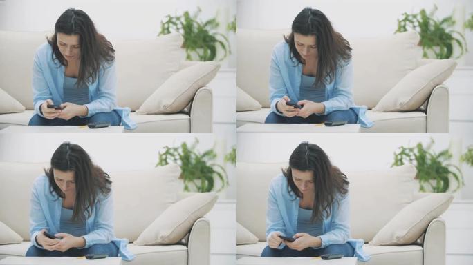 令人钦佩的女人正专注于在家中坐在沙发上使用智能手机。慢动作。复制空间。4K。