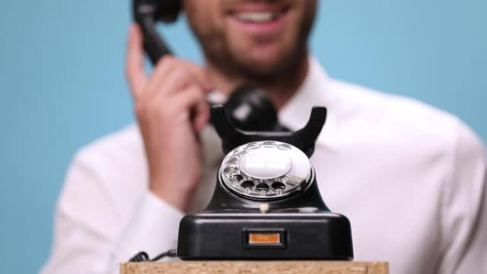 在一部老式电话上特写，一位年轻商人笑着回答，挂断电话，在蓝色背景上竖起大拇指