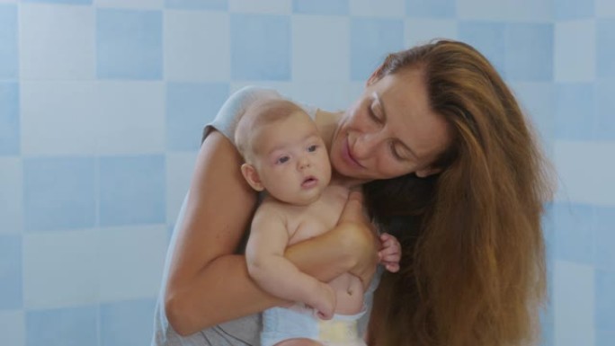 慈爱温柔的年轻妈妈抱着可爱的可爱的女婴女儿拥抱亲吻的小孩。快乐深情的母亲抱着婴儿，站在家里。