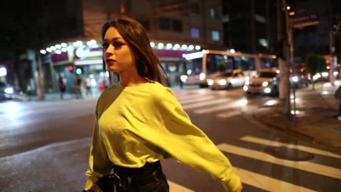 年轻女子晚上过马路。漂亮女孩在慢动作中行走在城市
