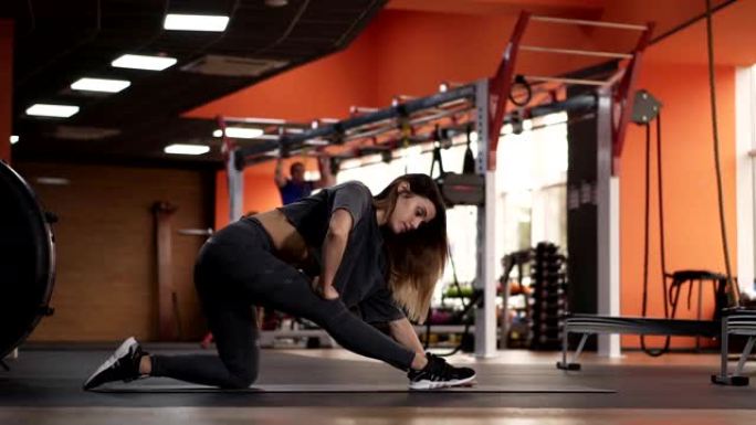 灵活的欧洲女性练习瑜伽姿势，并在健身房用运动器材做伸展运动。苗条的女孩做呼吸运动，在垫子上伸展身体。