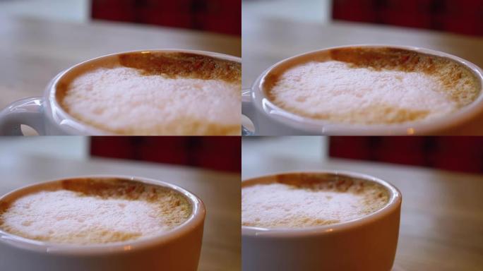 在餐厅的木桌上放着一杯带有白色泡沫的卡布奇诺咖啡。特写