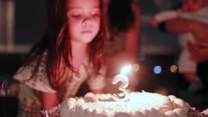 小女孩在庆祝三岁的生日蛋糕上吹蜡烛