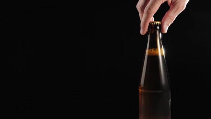 新鲜啤酒。手从黑色背景下的木制桌子上拿出一个棕色的瓶子，里面装着美味的精酿啤酒。水滴冷新鲜啤酒。准备