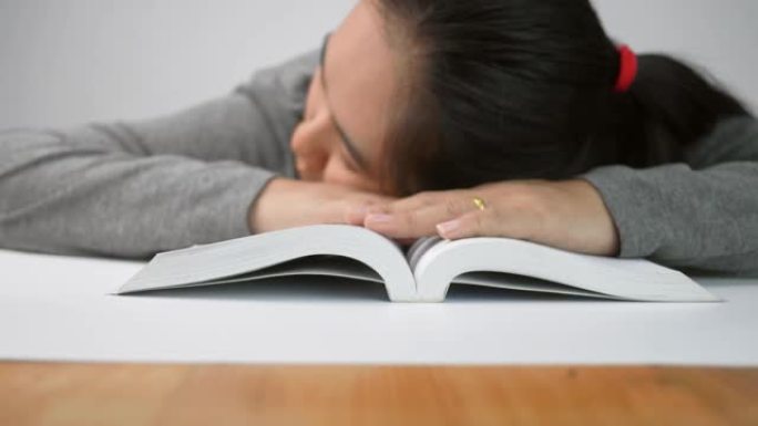 疲倦的学生女孩睡在家里的书本上。