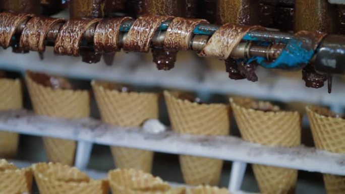 机器人机器会自动将巧克力倒入威化饼杯中。用于生产冰淇淋蛋筒的输送机自动线。威化杯和圆锥体。大型工业生