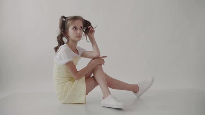 一个扎着马尾辫的女孩坐着，用手指若有所思地扭着头发。