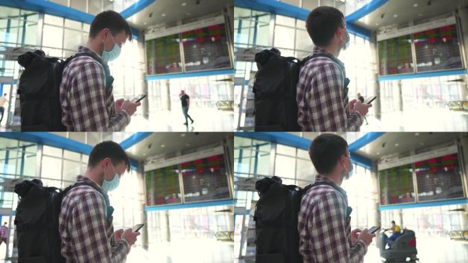 戴着口罩的男子游客在机场航站楼使用智能手机从抵达离境板检查航班。旅行时冠状病毒 (新型冠状病毒肺炎)