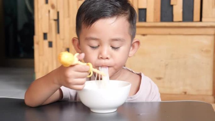 亚洲男孩正在用练习用儿童筷子吃面条。