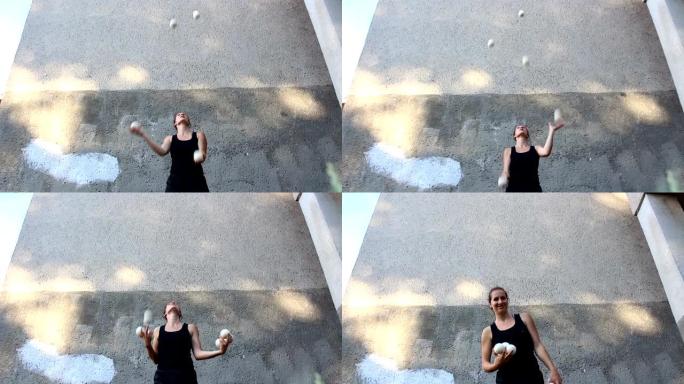 一个专业的马戏团女演员在街上玩白球。一个专业的杂耍演员玩白球。一个有魅力的女杂耍演员训练她的杂耍技巧