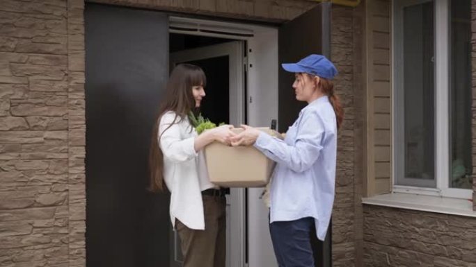 杂货店送货，年轻女子拿起在网上商店订购的一盒杂货，通过快递将女性送到家中