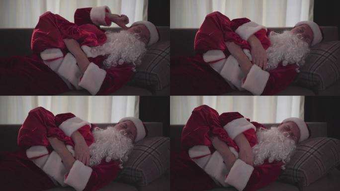 醉酒的老人，假白胡子，穿着圣诞老人的服装，睡在家里的沙发上，抱着礼物的包。坏圣诞老人。酗酒，消极主义