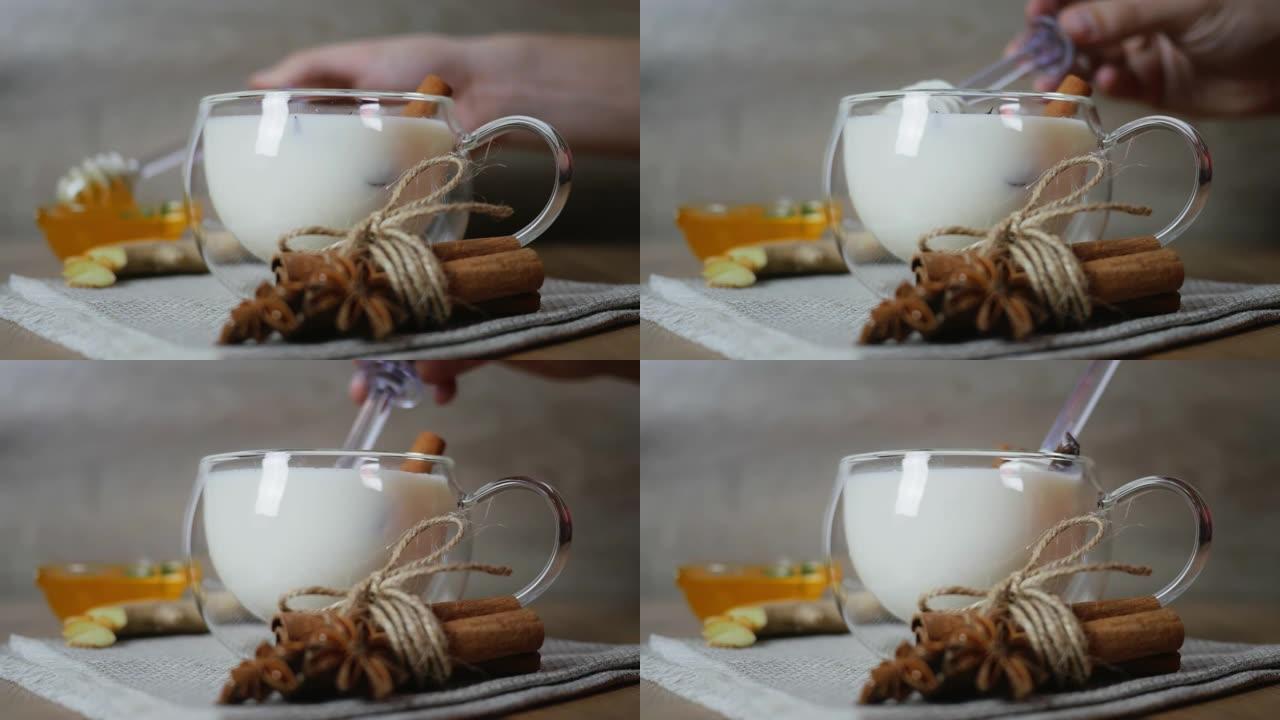 在传统印度马萨拉柴茶的杯杯中加入蜂蜜。印度马萨拉柴茶香料茶与牛奶在质朴的木制背景，选择性聚焦，复制空