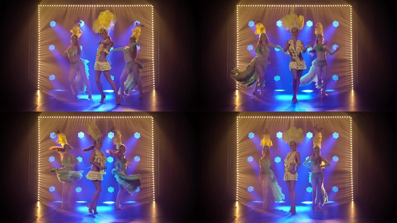三位火热的女舞者穿着带有羽毛的巴西狂欢节服装跳舞。带有动态霓虹灯的戏剧女性舞蹈表演。慢动作