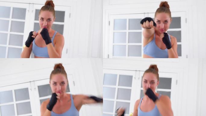 中枪的美丽运动女人正在练习拳击，她用严肃的脸向前猛击。自信的女人向空中挥拳练习拳击，独自在公寓锻炼。