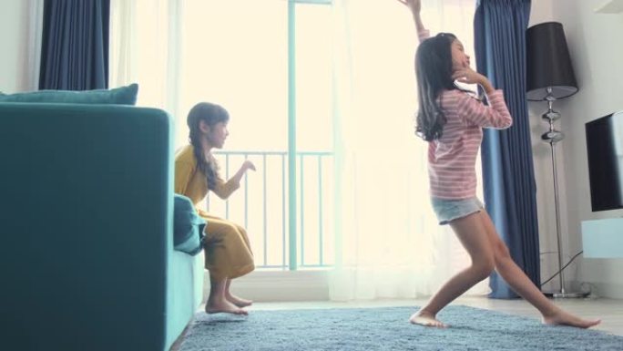 亚洲女性儿童兄弟姐妹在客厅一起玩乐。姐妹在沙发上一起跳舞。家庭在家里。人的概念