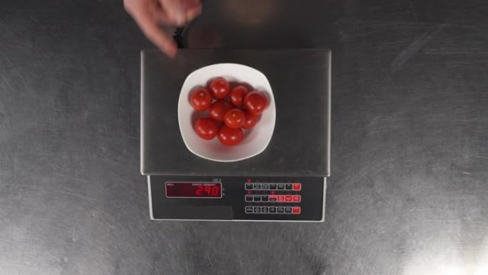 男性手将装有樱桃番茄的碗放在电子秤上称重。准备烹饪膳食食品的配料。健康食品概念