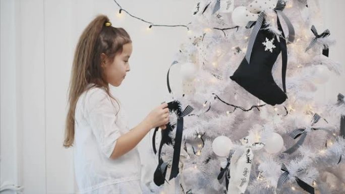 美丽的小女孩认为在圣诞树上悬挂条纹蝴蝶结和白球的地方。
