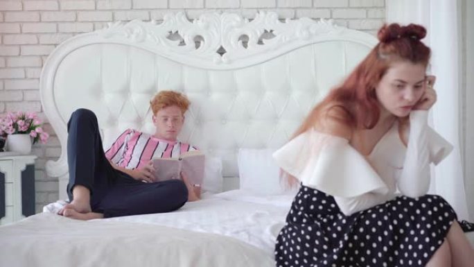 吸收英俊的红发男人躺在床上看书，像模糊的年轻悲伤的女人坐在前面思考。男朋友忽视美丽的女朋友。关系问题