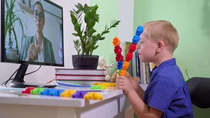 大流行期间的远程学习，患有唐氏综合症的男生在与她的女老师坐在家里用电脑学习时玩彩色玩具