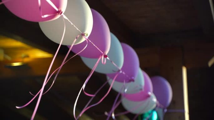 五彩氦气球挂在长绳上，在户外风中移动。各种气球装饰房屋或墙壁、生日或婚礼派对概念
