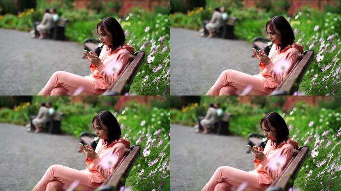 年轻女子坐在公园的长凳上，用智能手机翻转新闻。成年女性在新鲜空气中享受手机休息
