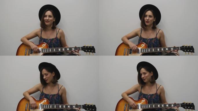 女性唱歌和弹吉他。唱抒情歌的女人。戴着帽子的年轻漂亮女孩情绪激动地唱歌和练习在白色背景下弹吉他