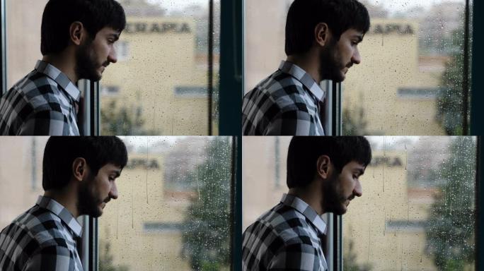 在雨天，窗户上的年轻悲伤的人迷失了自己的思想