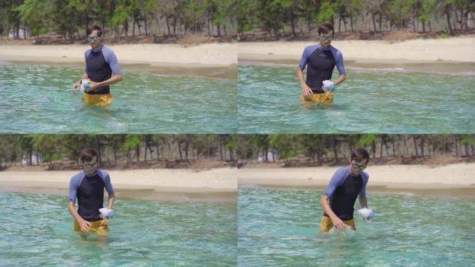 在美丽的绿松石海中收集塑料袋的男子的手持照片。天堂海滩污染。人为污染造成的沙滩上的垃圾问题。清洁环境
