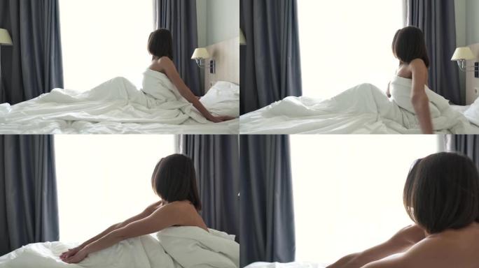 一个年轻漂亮的黑发女孩在床上醒来。女孩在白色的床上尽情享受。鸟瞰图。4k分辨率