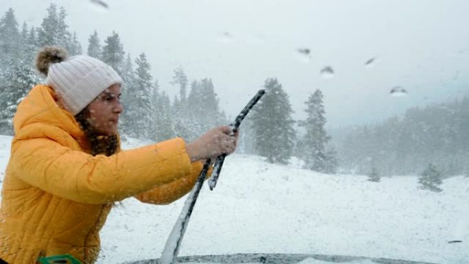 驾驶员的POV在中午在积雪覆盖的道路上行驶，第一场雪落下。暴风雪和降雪。年轻女子从冰上清洁挡风玻璃刮