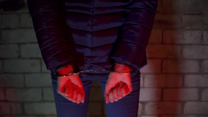 被捕的女人戴着手铐。戴着手铐的女性双手被警察的闪光器照亮。闪烁着蓝色和红色。