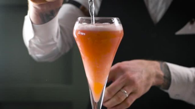 夜间酒吧的特写镜头。酒保将成品鸡尾酒倒入玻璃杯中。美丽的饮料供应在行业中很重要