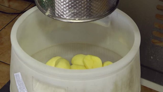 食品加工机械制造商。马铃薯去皮自动线。去皮的土豆掉进塑料桶里。