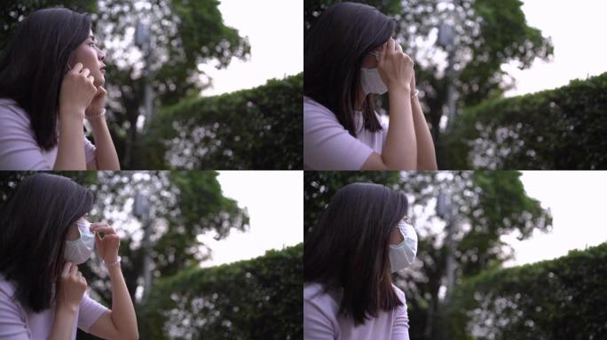 4k亚洲年轻女子戴着口罩坐下来，防止病毒传播，树荫下的绿叶灌木丛，covid19日冕病毒大流行，医疗